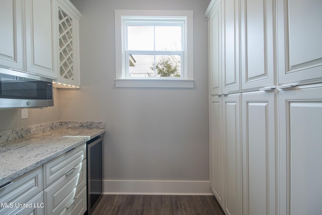 kitchen with beverage cooler, white cabinetry, light stone counters, and dark wood-type flooring