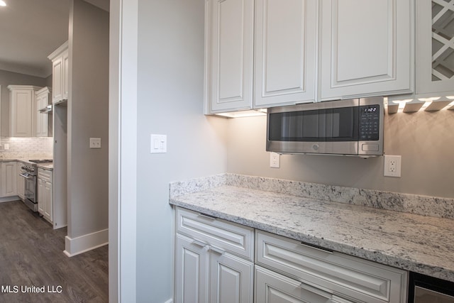 kitchen with dark wood-type flooring, stainless steel appliances, light stone countertops, white cabinets, and tasteful backsplash