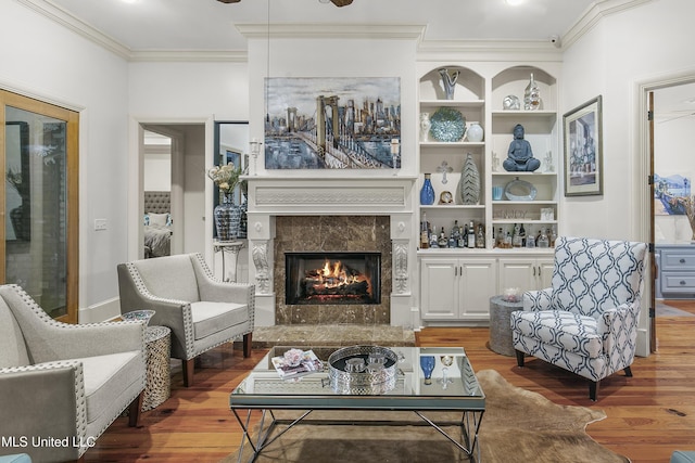 living room with wood-type flooring, built in features, ornamental molding, and a premium fireplace