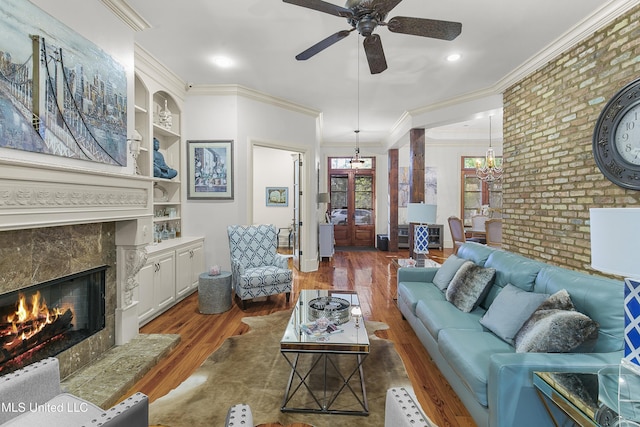 living room with a high end fireplace, ornamental molding, built in shelves, ceiling fan, and dark wood-type flooring