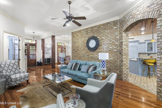 living room featuring ceiling fan, crown molding, dark wood-type flooring, and brick wall