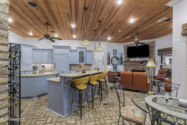 kitchen with light stone countertops, a kitchen island with sink, gray cabinetry, and hanging light fixtures