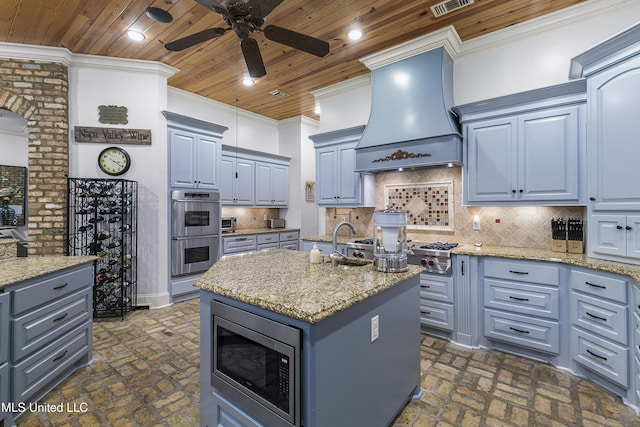 kitchen with premium range hood, a center island with sink, decorative backsplash, ceiling fan, and stainless steel appliances