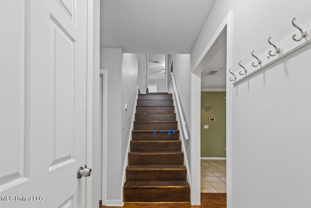 staircase featuring baseboards, tile patterned floors, visible vents, and a textured ceiling
