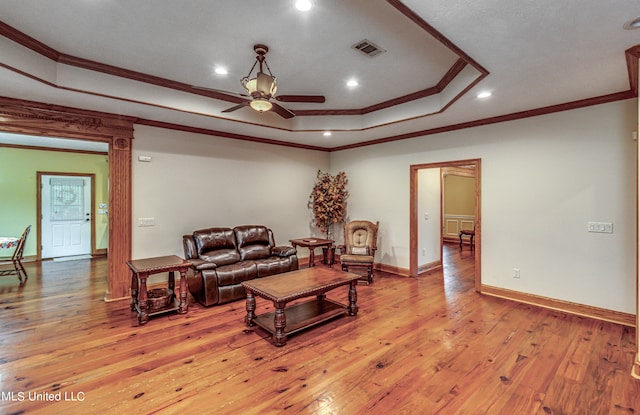 living room with crown molding, a tray ceiling, light wood-type flooring, and ceiling fan