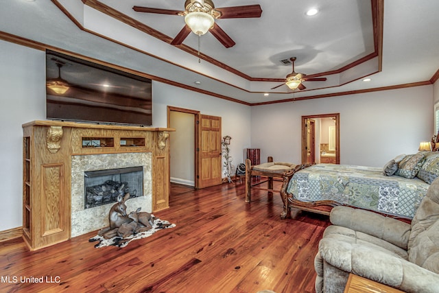 bedroom featuring a raised ceiling, a high end fireplace, ceiling fan, dark wood-type flooring, and crown molding