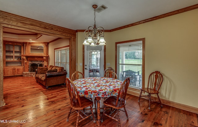 dining area with hardwood / wood-style flooring, ornamental molding, a brick fireplace, and a chandelier