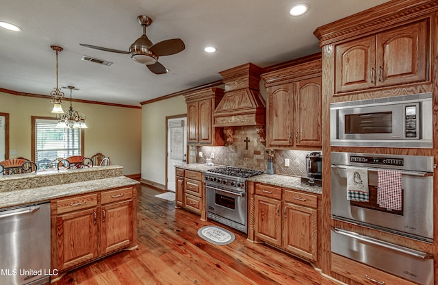 kitchen featuring light hardwood / wood-style flooring, hanging light fixtures, stainless steel appliances, crown molding, and light stone countertops