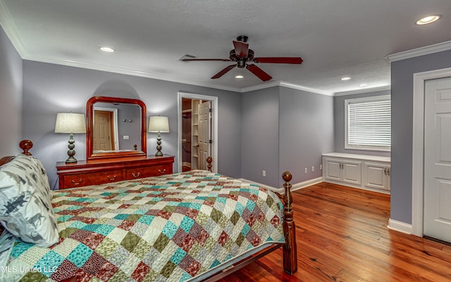 bedroom with ceiling fan, hardwood / wood-style flooring, ornamental molding, and a walk in closet