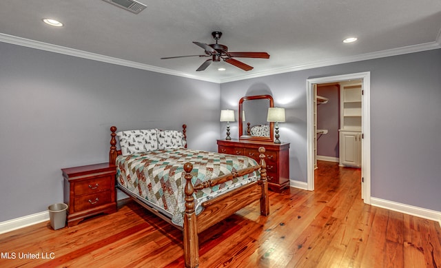 bedroom featuring hardwood / wood-style flooring, a closet, a walk in closet, crown molding, and ceiling fan