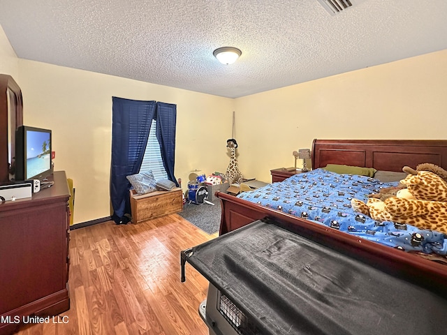 bedroom with baseboards, visible vents, light wood-style flooring, and a textured ceiling