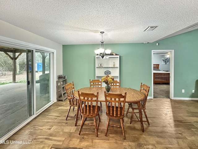 dining space featuring wood finished floors, visible vents, a textured ceiling, and an inviting chandelier