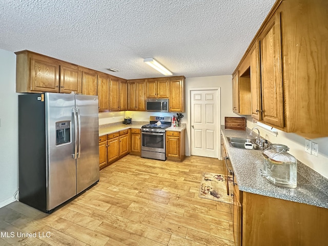 kitchen with a textured ceiling, light wood-style flooring, stainless steel appliances, a sink, and brown cabinets