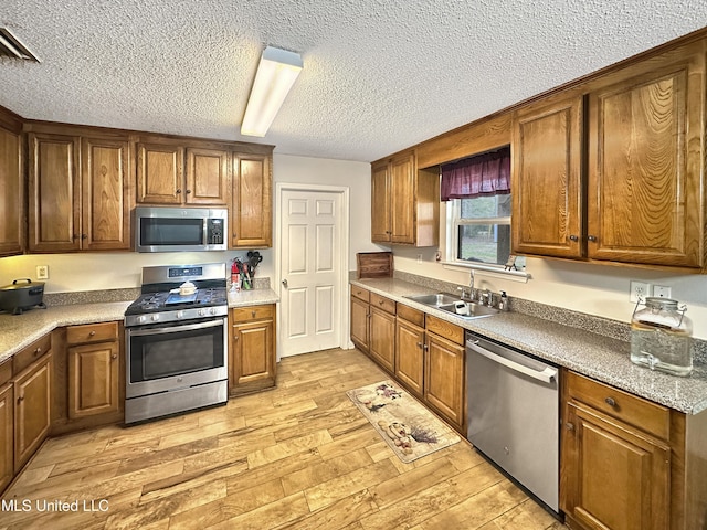 kitchen with stainless steel appliances, brown cabinets, a sink, and light wood finished floors