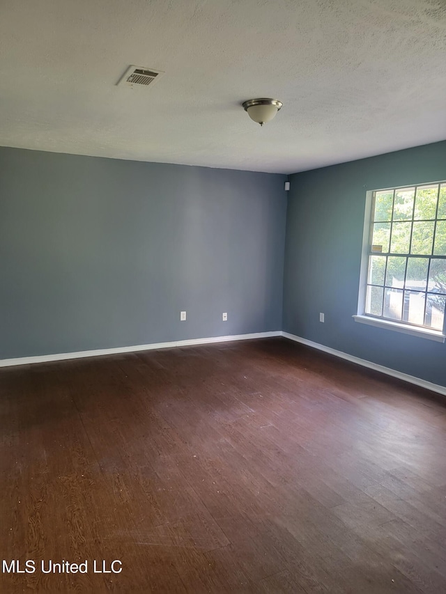 spare room featuring a textured ceiling and dark hardwood / wood-style floors