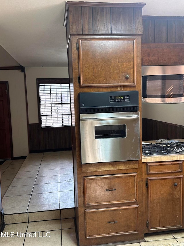 kitchen featuring stainless steel appliances, light tile patterned floors, and wood walls