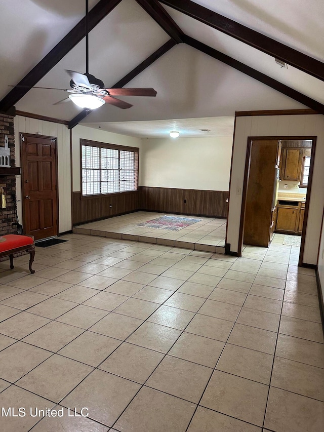 unfurnished living room featuring wooden walls, vaulted ceiling with beams, light tile patterned floors, and ceiling fan