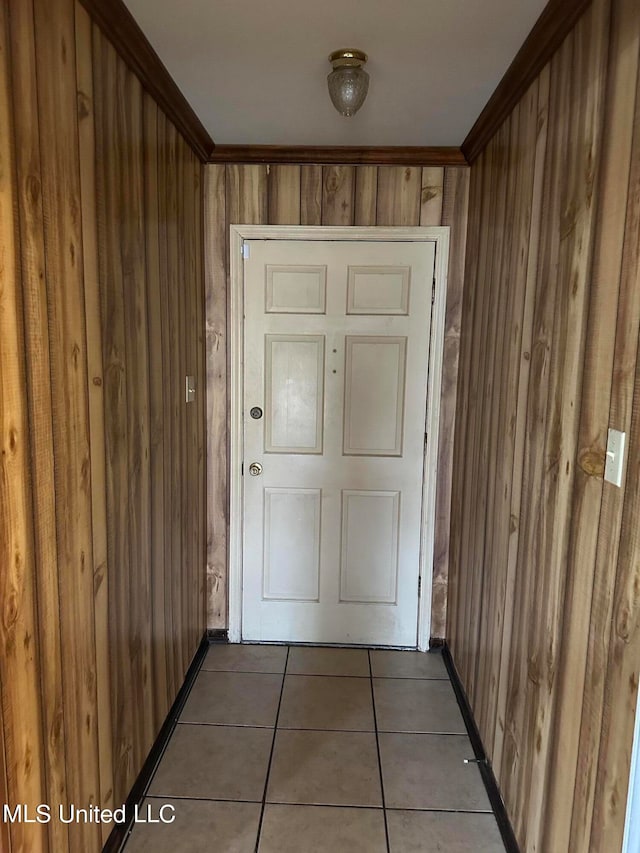 doorway to outside with wooden walls, crown molding, and tile patterned flooring