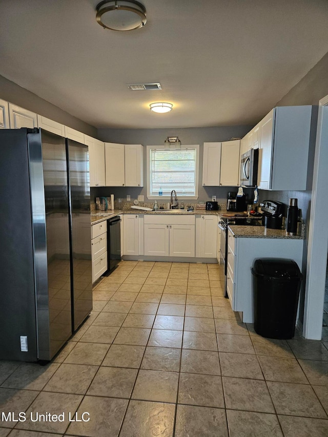 kitchen with dark stone countertops, sink, black appliances, light tile patterned floors, and white cabinetry