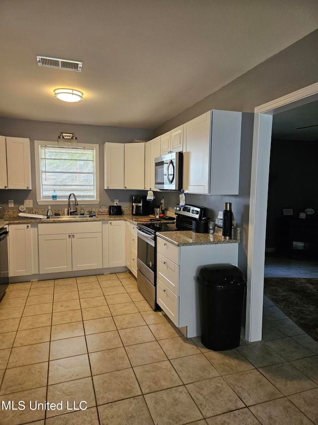 kitchen with appliances with stainless steel finishes, light tile patterned flooring, sink, white cabinetry, and dark stone counters