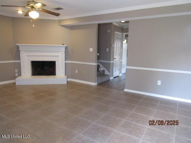 unfurnished living room featuring tile patterned flooring, crown molding, a brick fireplace, and ceiling fan