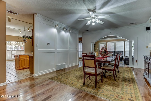 dining room featuring track lighting, ornamental molding, a textured ceiling, ceiling fan, and light hardwood / wood-style floors