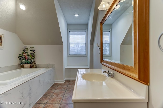 bathroom with vaulted ceiling, vanity, a relaxing tiled tub, and a textured ceiling