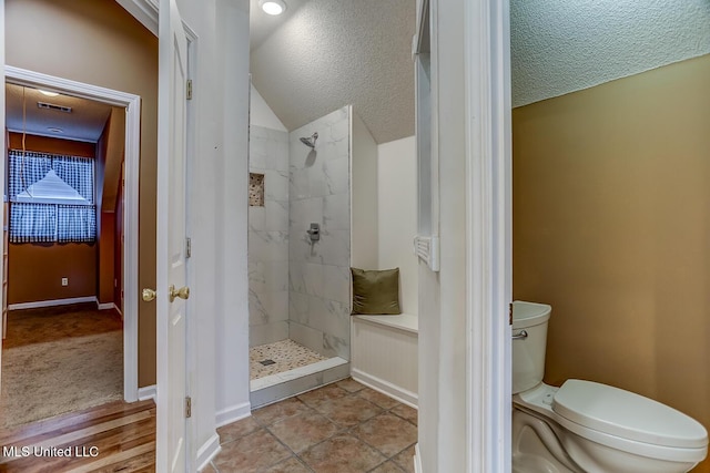 bathroom featuring tile patterned floors, a tile shower, a textured ceiling, vaulted ceiling, and toilet