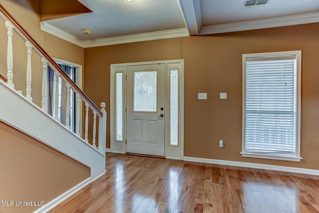 foyer with light wood-type flooring, a textured ceiling, and ornamental molding