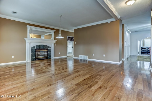 unfurnished living room featuring a tiled fireplace, light hardwood / wood-style flooring, a textured ceiling, and ornamental molding