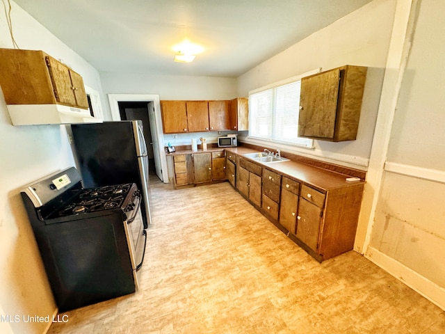 340 Elm Ave, Clarksdale, MS 38614 - kitchen featuring appliances with stainless steel finishes, a sink, brown cabinetry, light flooring, and under cabinet range hood