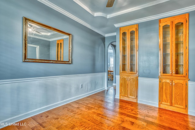 spare room with arched walkways, wood finished floors, crown molding, and a wainscoted wall
