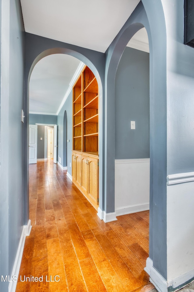corridor featuring ornamental molding, arched walkways, wood finished floors, and baseboards