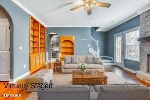 living room with arched walkways, a fireplace, built in features, baseboards, and a ceiling fan