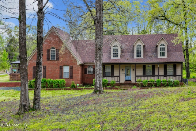 view of front of house with covered porch, a front yard, roof with shingles, and brick siding