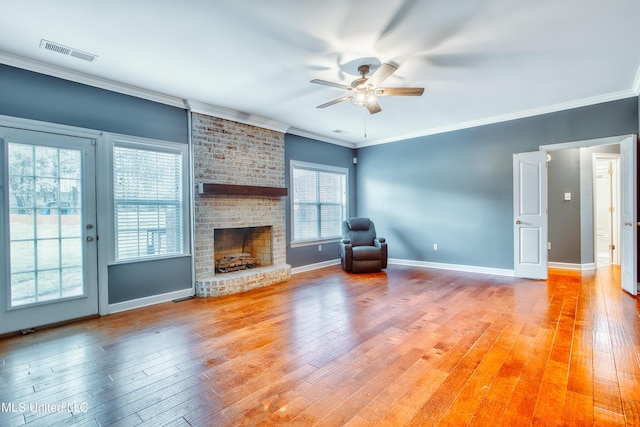 unfurnished living room with a ceiling fan, light wood-type flooring, crown molding, a brick fireplace, and baseboards