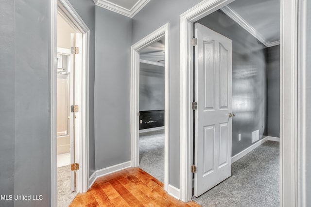 corridor with light carpet, crown molding, baseboards, and light wood-type flooring
