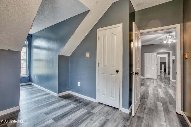 additional living space featuring a textured ceiling, lofted ceiling, wood finished floors, baseboards, and ceiling fan