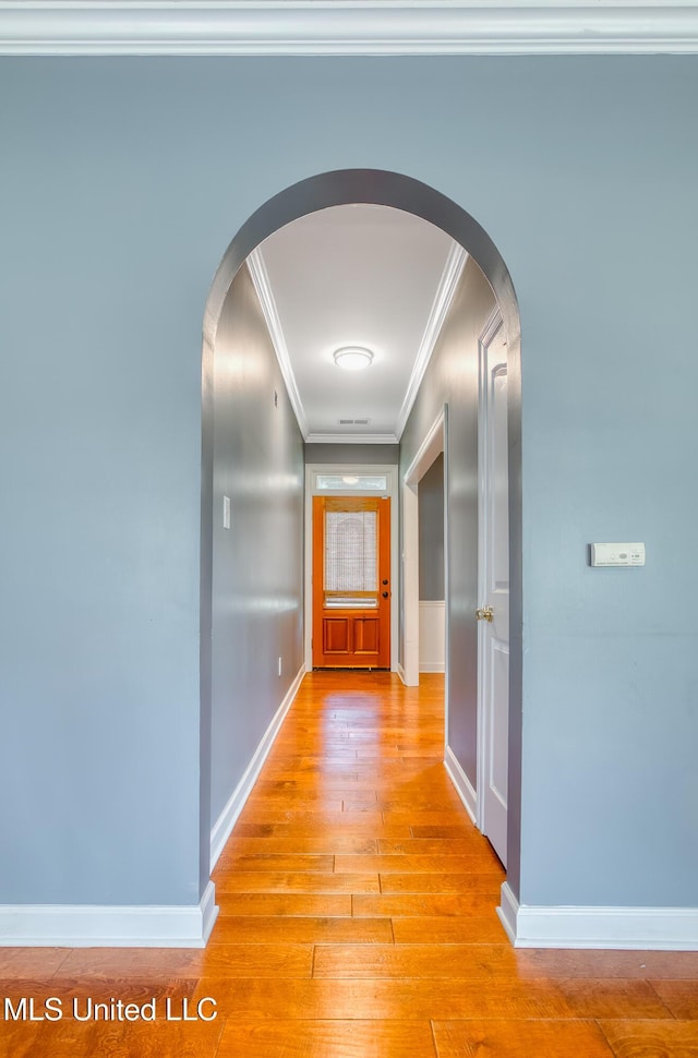 hall with arched walkways, crown molding, light wood finished floors, and baseboards