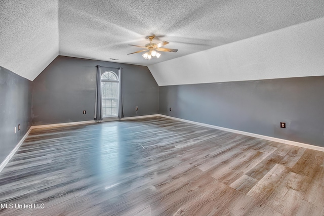 bonus room with a ceiling fan, a textured ceiling, vaulted ceiling, baseboards, and wood finished floors