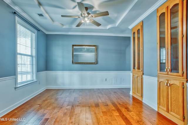 empty room with light wood finished floors, ceiling fan, and a tray ceiling