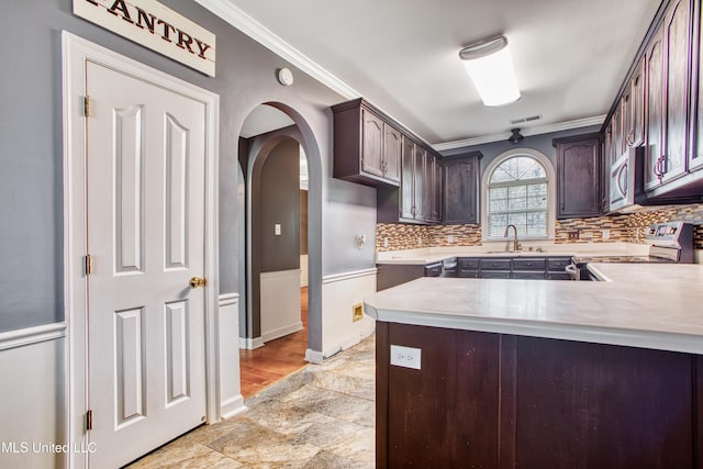 kitchen featuring stainless steel appliances, ornamental molding, a sink, dark brown cabinets, and arched walkways