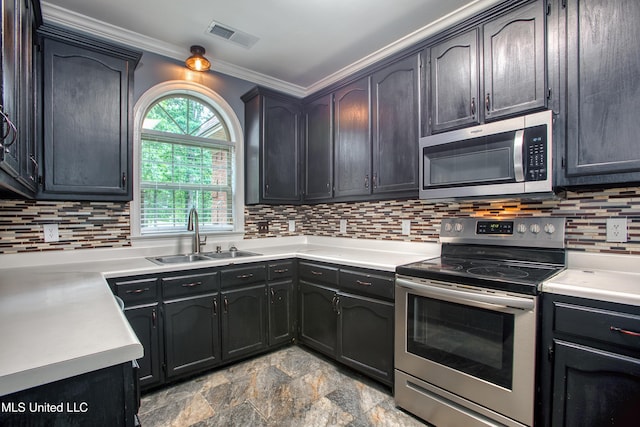 kitchen with stainless steel appliances, a sink, ornamental molding, backsplash, and stone finish floors