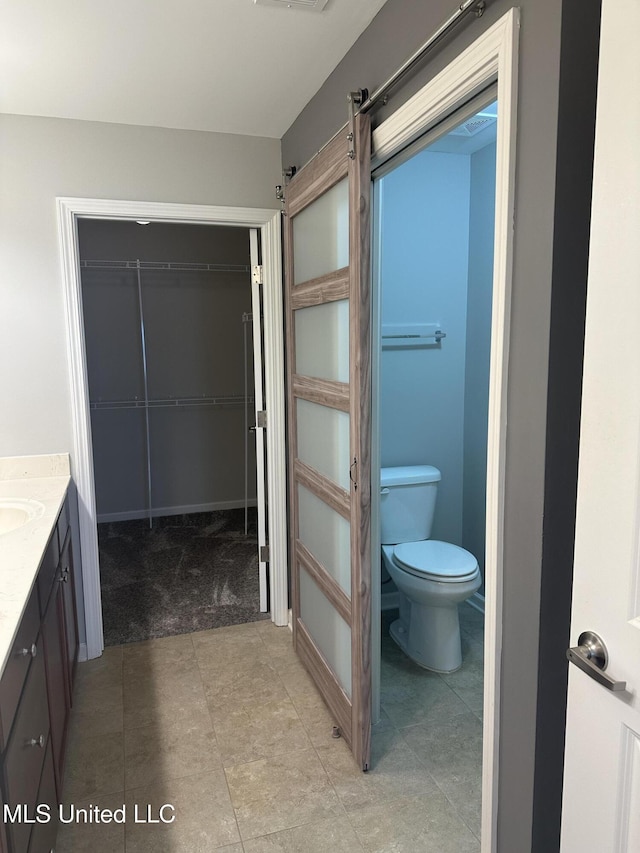 bathroom featuring a spacious closet, toilet, and vanity