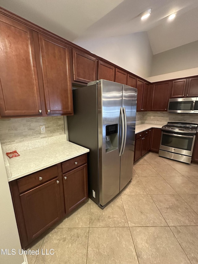 kitchen with vaulted ceiling, appliances with stainless steel finishes, light countertops, and light tile patterned flooring