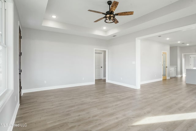 spare room with light wood-style flooring, a tray ceiling, baseboards, and recessed lighting