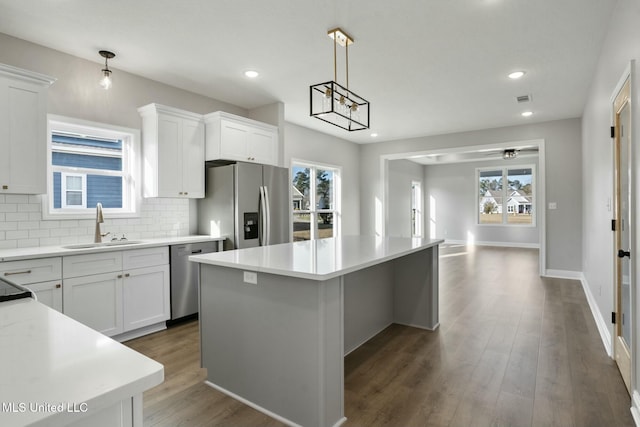 kitchen featuring stainless steel appliances, a kitchen island, a sink, decorative backsplash, and dark wood finished floors