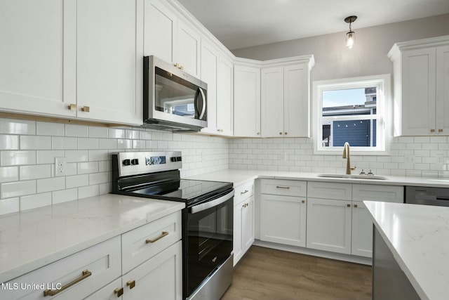 kitchen with tasteful backsplash, white cabinets, appliances with stainless steel finishes, wood finished floors, and a sink