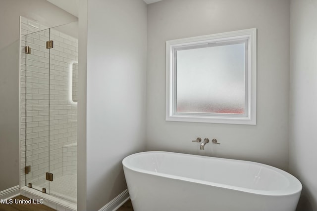 full bathroom with a stall shower, a soaking tub, and baseboards