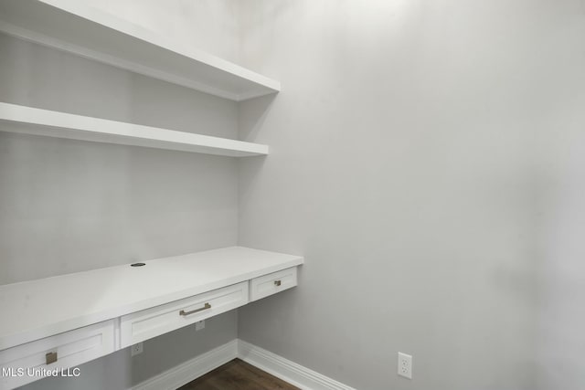 unfurnished office featuring dark wood-type flooring, built in desk, and baseboards